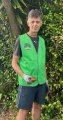 White man with grey hair standing with a hi vis vest on in the bush