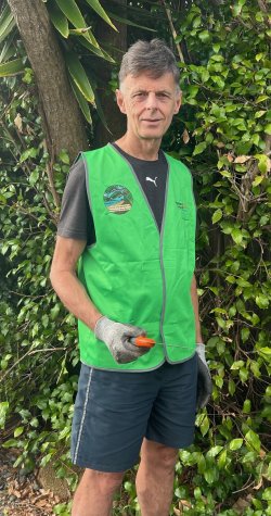 White man with grey hair standing with a hi vis vest on in the bush