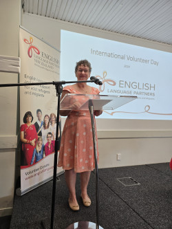 GM, in orange dress, standing behind a lectern with ESOL banner behind