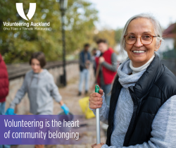 smiling older woman holding a rake volunteering at a clean up on the beach