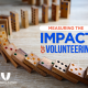 Dominoes lined and with the first ones falling. sign saying measuring the impact of volunteering