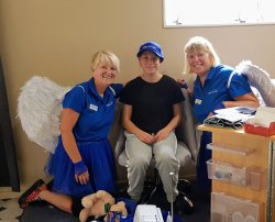 Anika is sitting on a chair in front of her new sewing machine with Janet and Carol on each side of her. All are smiling.