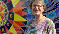 A woman standing and smiling beside a colourful mosaic wall