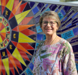 A woman standing and smiling beside a colourful mosaic wall