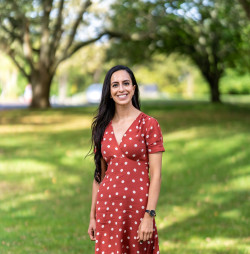 Ruchika is smiling and standing in a park wearing a red dress